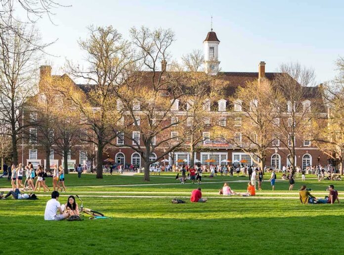 shutterstock_1037739901-1 Students relaxing on a campus quad in front of a brick academic building