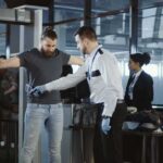 14,000 Security Guards Threaten Tech Strike airport security officer wands traveler at metal detector