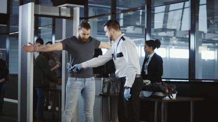 airport security officer wands traveler at metal detector