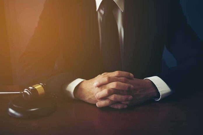 shutterstock_1049502869-1 person in suit with hands clasped at a desk beside a gavel