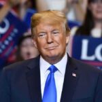 Donald Trump at a rally wearing a dark suit and blue tie