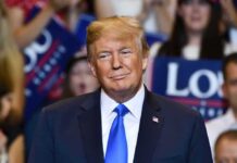 Donald Trump at a rally wearing a dark suit and blue tie