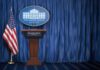 $810M Funding Cut Sparks Power Fight White House press briefing podium with U.S. flag and blue curtain