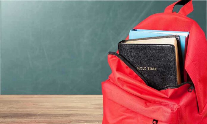 shutterstock_1183389583-1 Red backpack with books on a classroom desk
