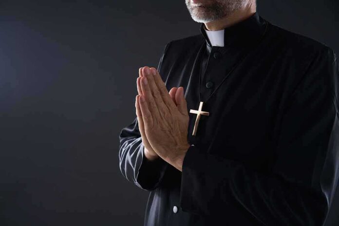 shutterstock_1212427192 Clergyman in black robe praying with hands together