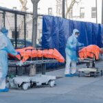 17 Americans AIRLIFTED and Quarantined! Healthcare workers in PPE move covered stretchers outside a facility
