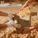Archaeologists cleaning a large stone artifact at a dig site