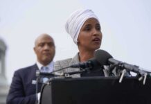 Ilhan Omar speaking at a podium with André Carson standing behind