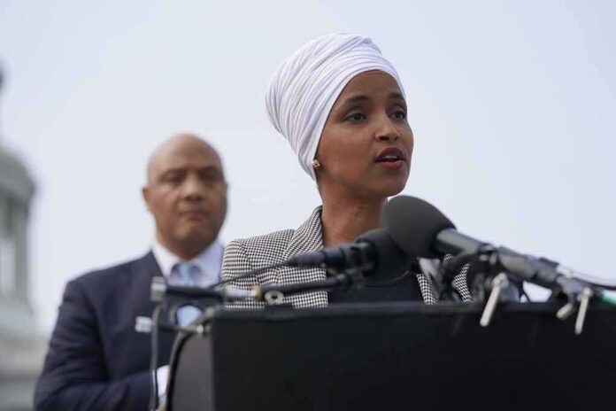 shutterstock_2012384414-2 Ilhan Omar speaking at a podium with André Carson standing behind
