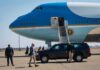 Security detail near blue and white aircraft with staircase and SUV