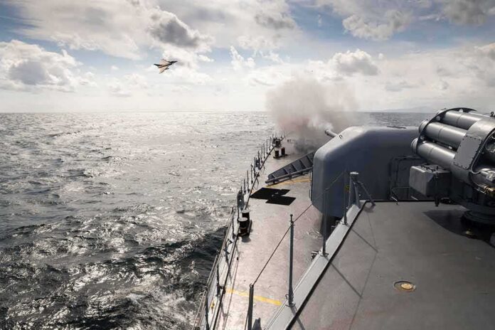 shutterstock_2129183807-1 naval warship firing deck gun at sea