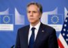 Gaza Inaction Accusation Sparks Debate Man in suit at press conference with EU and US flags behind