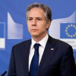 Man in suit at press conference with EU and US flags behind