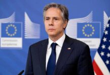 Gaza Inaction Accusation Sparks Debate Man in suit at press conference with EU and US flags behind