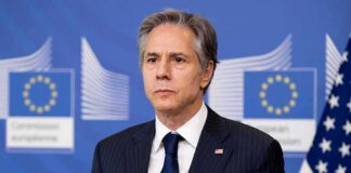 Man in suit at press conference with EU and US flags behind