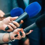 Forbes Editor Fired Over $6M Payment Reporters holding colorful microphones