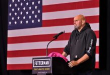 House Votes Again to Curb Iran War Powers Man in hoodie speaking at a podium before a large U.S. flag