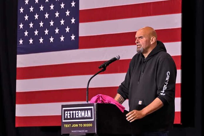 shutterstock_2206788177 Man in hoodie speaking at a podium before a large U.S. flag