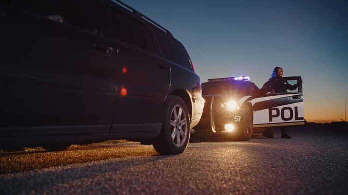 Police officer at patrol car during traffic stop at dusk