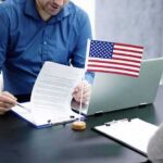Fauci Files Ignite Washington Firestorm Two people at a desk reviewing documents with a small American flag by a laptop