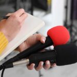 Trump’s Tribute to Victor Willis Sparks New Firestorm Journalist holding two microphones while writing in a notebook