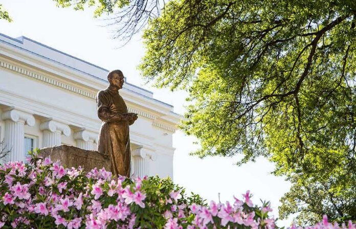 shutterstock_400931917 Bronze statue in a garden with pink flowers and a neoclassical building