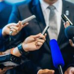 Man in suit surrounded by microphones at press conference