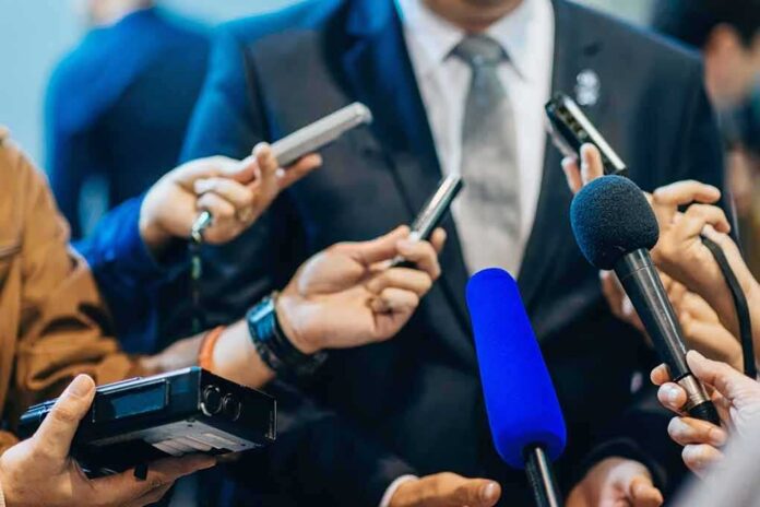 shutterstock_471987565 Man in suit surrounded by microphones at press conference