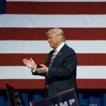 Donald Trump clapping on stage before a large American flag