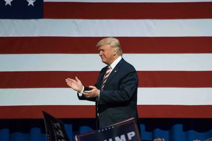 Donald Trump clapping on stage before a large American flag