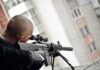 Person aiming a scoped rifle from a balcony