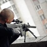 Person aiming a scoped rifle from a balcony