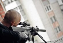 Person aiming a scoped rifle from a balcony