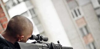 Person aiming a scoped rifle from a balcony