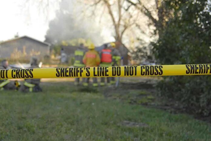 shutterstock_5838397-1 Yellow police tape marking a restricted area at a fire scene with firefighters in the background