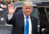 Donald Trump waves while standing beside a black vehicle