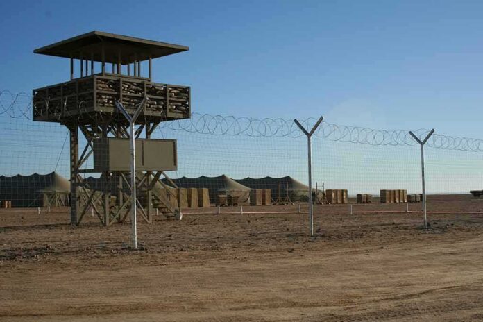 Guard tower beside barbed-wire fence in desert camp