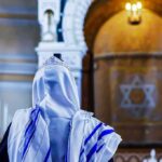 America’s Promise Shattered—Rabbi Walks Away Person in white and blue prayer shawl facing ornate interior
