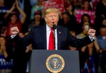 Trump Turns Question Into Media Brawl Donald Trump speaking at a rally podium with arms raised