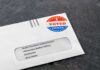 Trump Raises Election Fraud Fears Absentee ballot envelope with I Voted sticker on dark surface