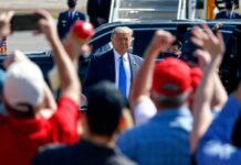 Man in suit greeted by crowd with raised hands