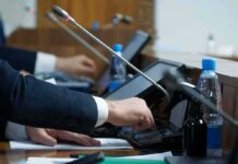 Memoir Reveals Cabinet Drama Person pressing a button on a conference microphone panel