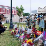 “Traitor” Chants Follow Mamdani at Vigil Police officer kneels at a memorial with flowers and crosses