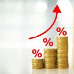 Stacks of coins with rising red arrow and wooden blocks spelling FED