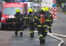 Firefighters walking toward a scene with hoses and a red emergency van