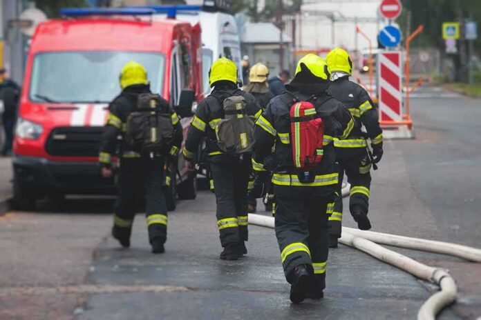 shutterstock_2358506065 Firefighters walking toward a scene with hoses and a red emergency van