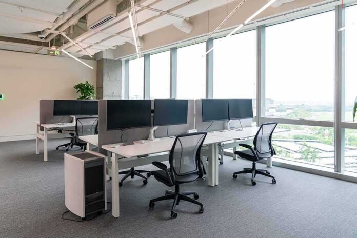 shutterstock_2470118869 Modern open-plan office with workstations by large windows