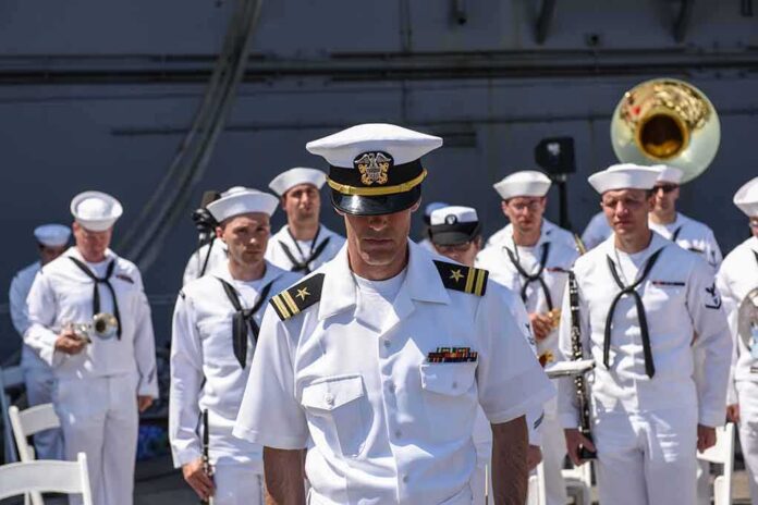 naval officer in white uniform stands before a military band