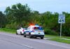 Police SUV with lights on behind a white car on roadside near 45 mph sign